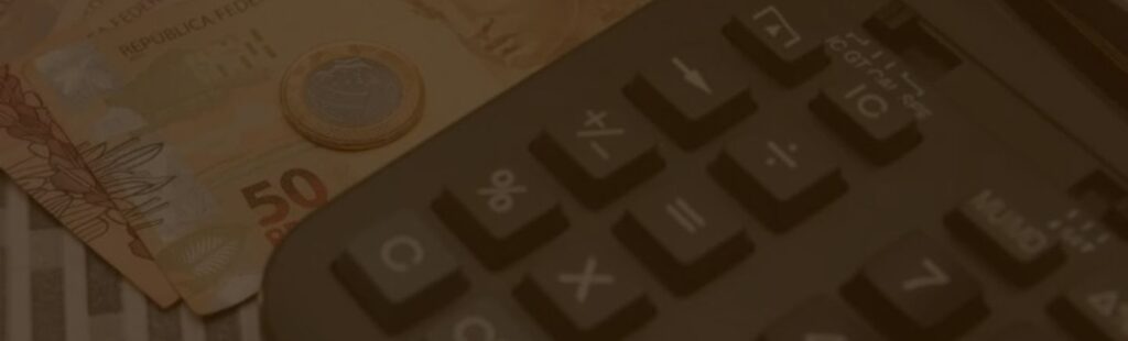 Notas de cinquenta reais e uma moeda de um real ao lado de uma calculadora, representando cálculos e finanças relacionadas à Reforma Tributária de 2023 no Brasil.